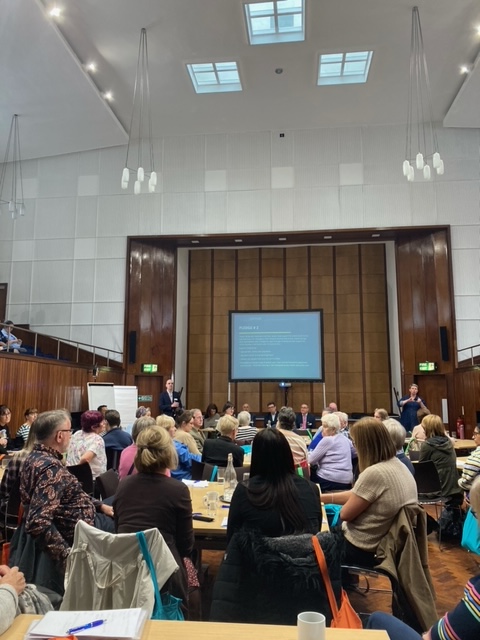 Greater Manchester Living Well with Dementia event. People sat around a large conference room with people sat at the front taking part in a panel discussion.